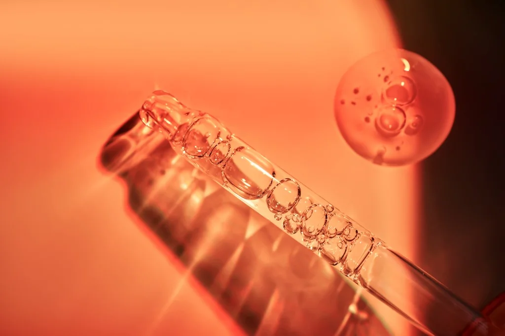 Pipette en verre et goutte de sérum sur fond orange lumineux, esthétique beauté et skincare