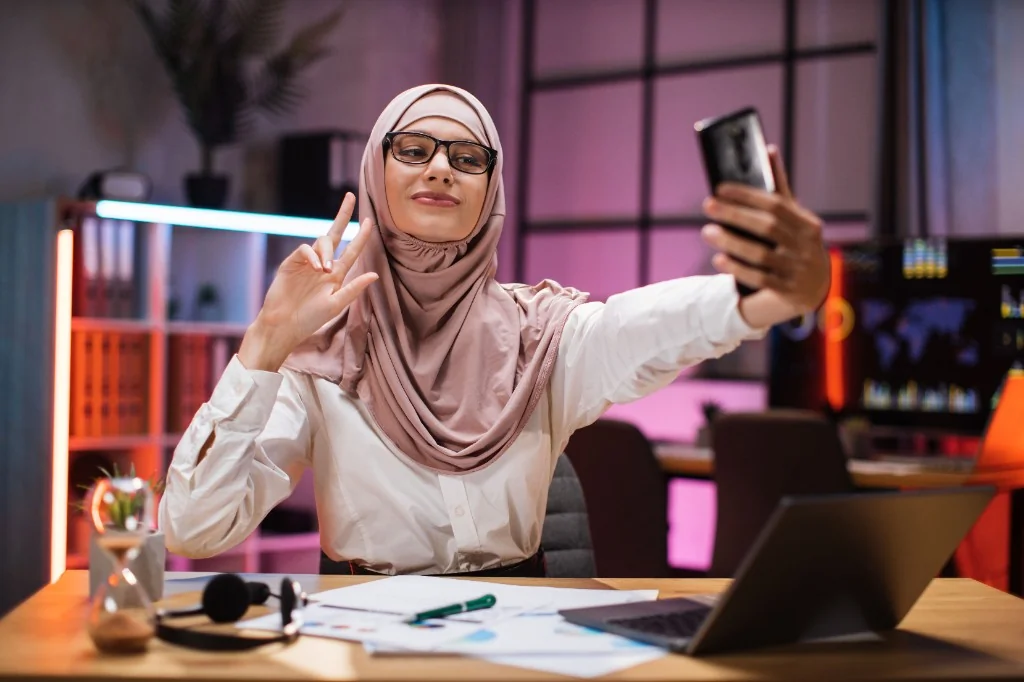 Créatrice de contenu en hijab, selfie au bureau, écran de données, collaboration marque